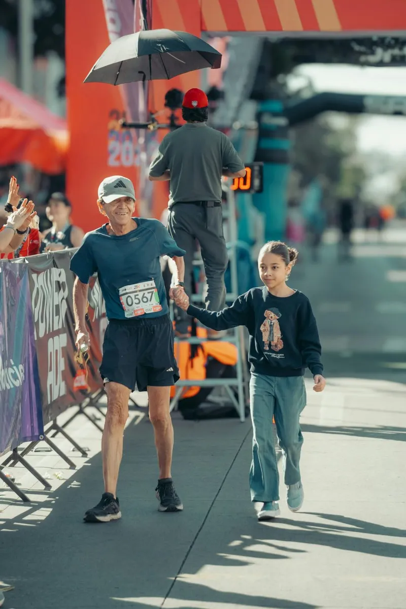 An older runner in a race bib walks hand in hand with a young girl toward the finish line of a road race
