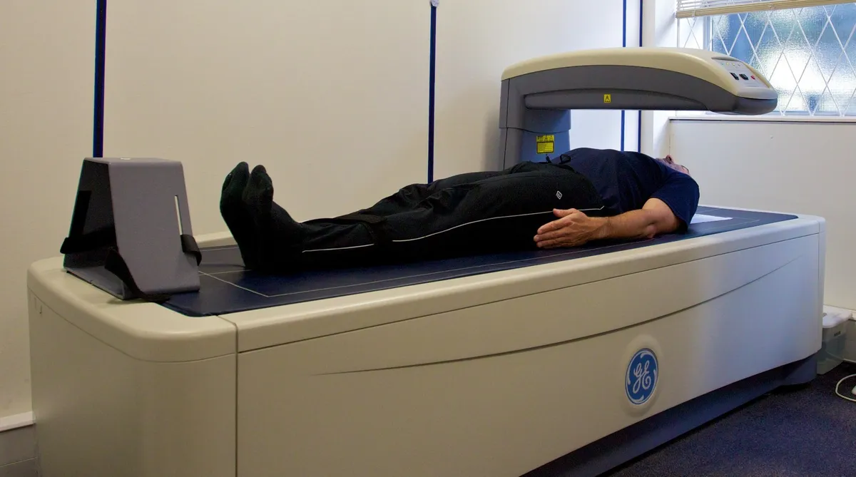 A DEXA scan in progress: a person lies on an open table while the scanner arm passes over them