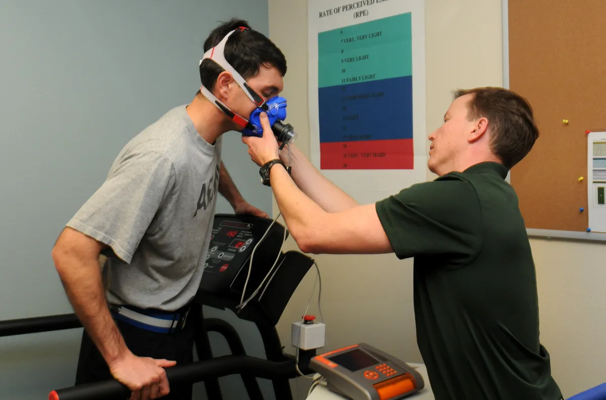 A technician fits a breathing mask on a soldier standing on a treadmill before a VO2 max test