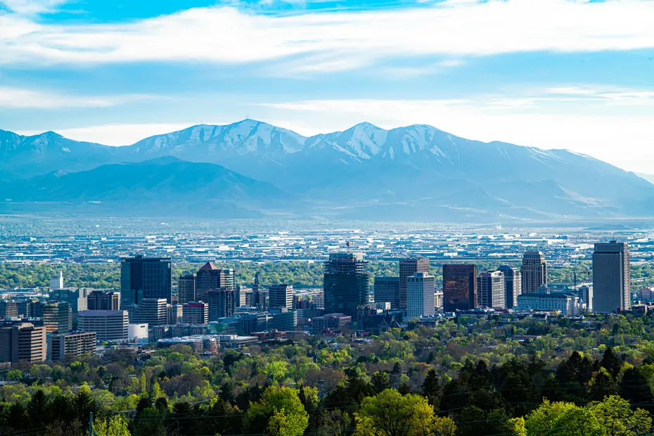 The Salt Lake City skyline above green trees, with snow-capped mountains behind it